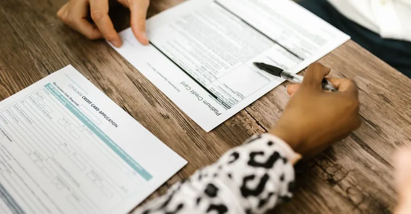 Close-up of two people reviewing and filling out a credit card application on a wooden table.