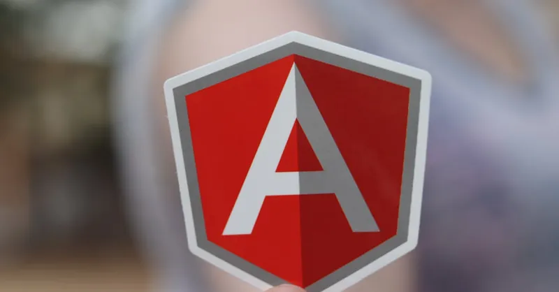 A person holding a red Angular logo sticker focusing on software development and security.